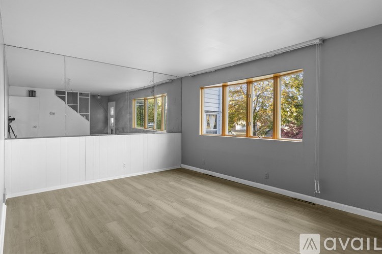 A spacious room with wooden flooring and a large window with a view of trees.