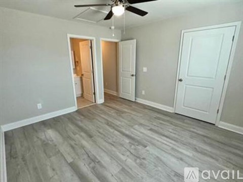 A room with a ceiling fan and light, two doors, and a wooden floor.