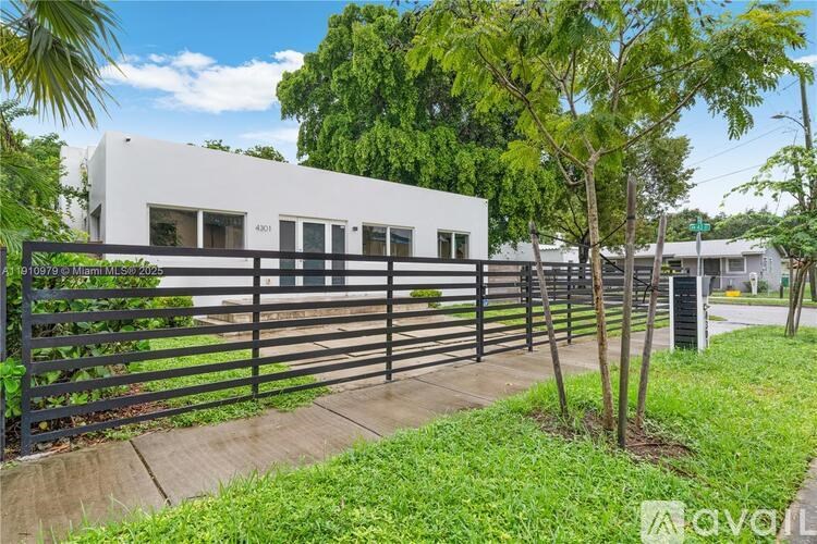 A white building with a black fence and a tree in front.