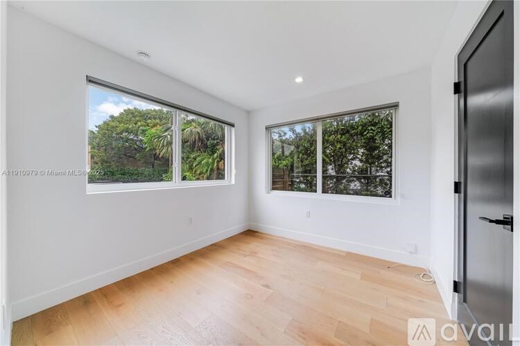 A spacious room with wooden floors and large windows overlooking a green landscape.