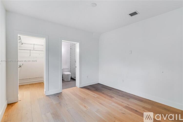 A room with wooden floors and white walls, with a window on the left and a door on the right.
