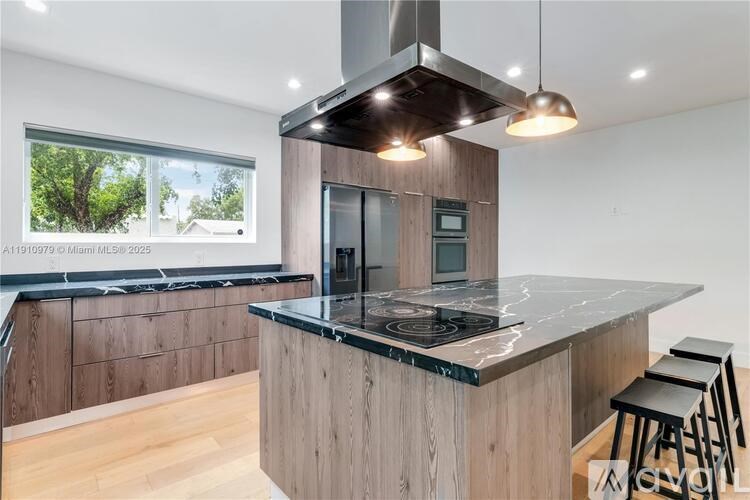 A modern kitchen with a large island and a view of trees outside the window.