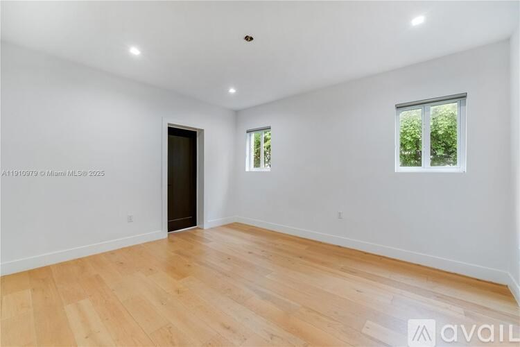 A spacious room with wooden flooring and two windows.