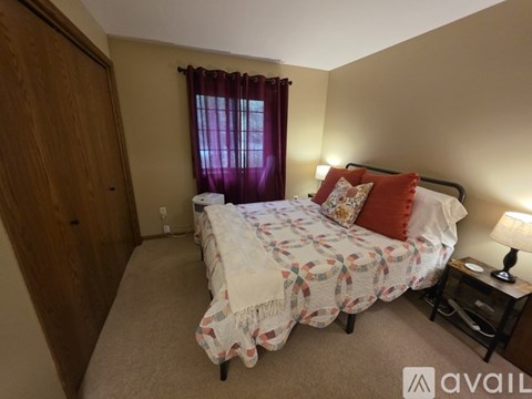 A bedroom with a bed, nightstand, and window with curtains.