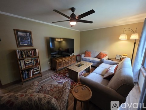 A living room with a ceiling fan, a couch, a coffee table, and a bookshelf.