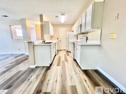 A kitchen with white cabinets and wooden floors.
