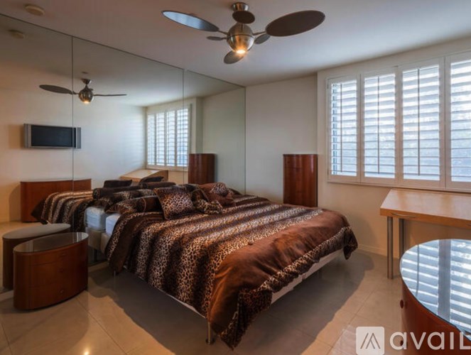 A bedroom with a bed covered in a leopard print blanket, a ceiling fan, and a television.