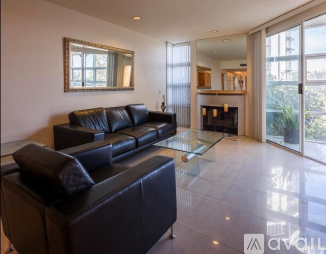 A black leather sofa sits in a spacious living room with a glass coffee table.