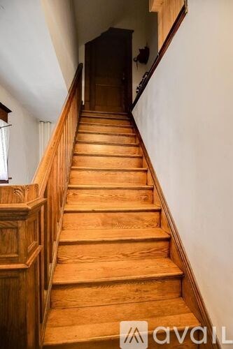 A wooden staircase with a white wall on one side and a wooden door on the other.