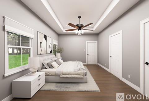 A bedroom with a large bed, a ceiling fan, and a window with a view of a lawn.