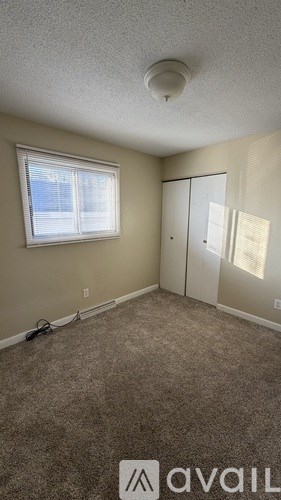 A room with a carpeted floor, a window with blinds, and a white ceiling with a smoke detector.