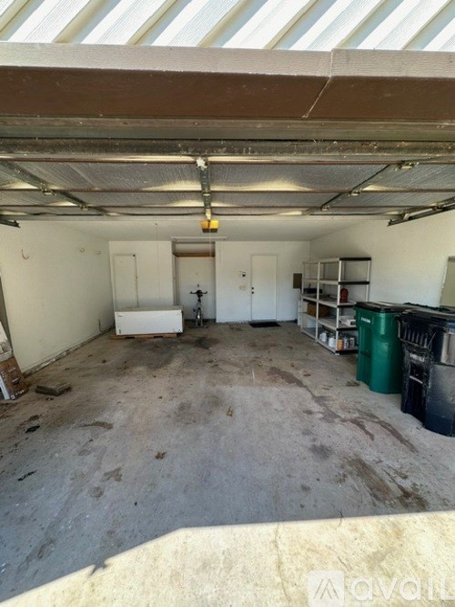 A large, empty warehouse with a white ceiling and walls, and a few pieces of furniture and bins scattered around.