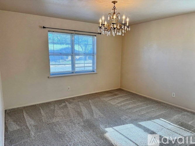 A room with a chandelier, carpeted floor, and a window with blinds.