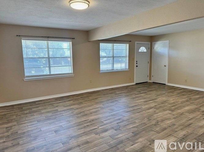 A spacious room with wooden flooring and two windows.