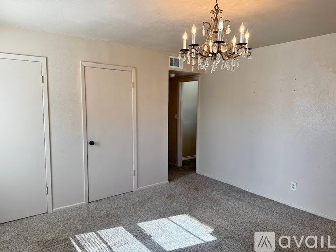 A room with a chandelier, two doors, and a carpeted floor.