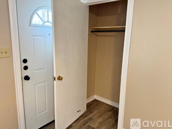 A white door with a black handle and a gold lock is open to a small, empty closet.