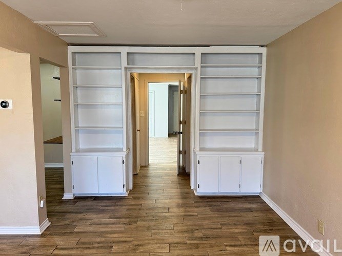 A hallway with white cabinets and a wooden floor.