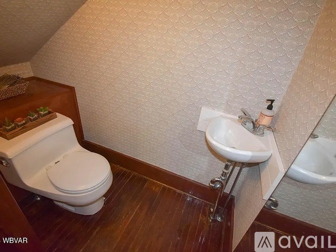 A bathroom with a toilet, sink, and wooden floors.