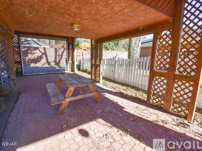 A wooden bench is on a brick patio under a wooden lattice.