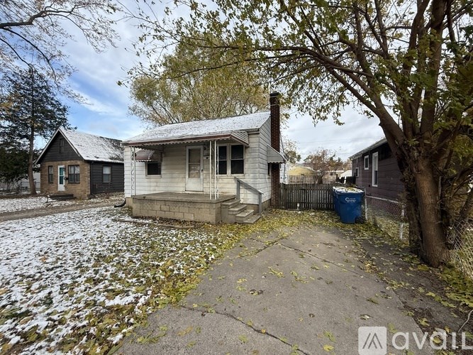 A house with a snow-covered roof and a blue trash bin in front.