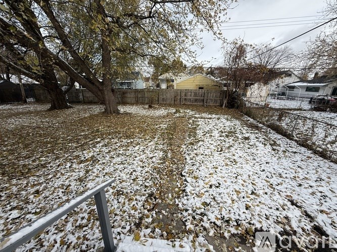 A backyard with a fence and a tree with snow on the ground.