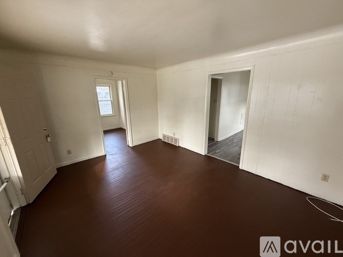 A room with wooden floors and white walls, with a door on the right side.