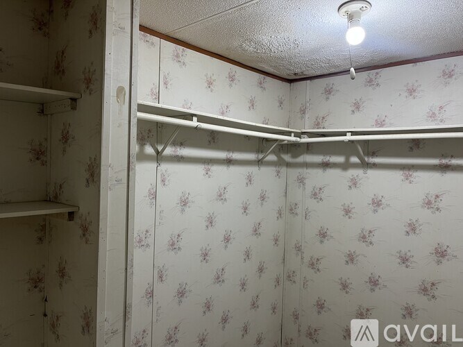 A small, empty room with floral wallpaper and a single light bulb on the ceiling.
