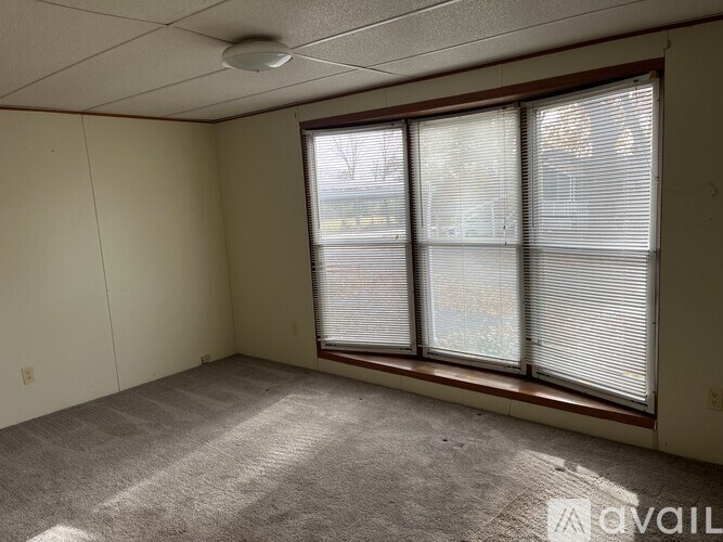 A room with a carpeted floor, a window with blinds, and a ceiling light fixture.