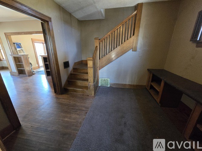 A room with wooden stairs and a grey carpet.