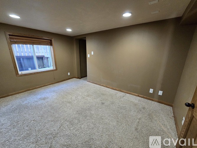 A room with a carpeted floor, a window with blinds, and a door.