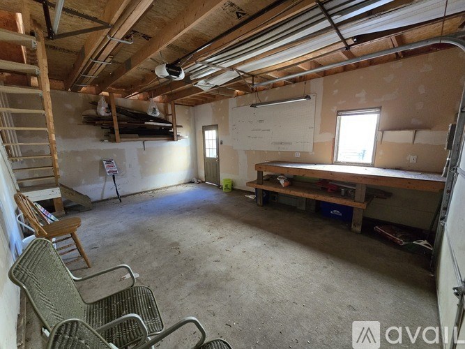 A room with a workbench and chairs is under construction with exposed pipes and wooden beams.