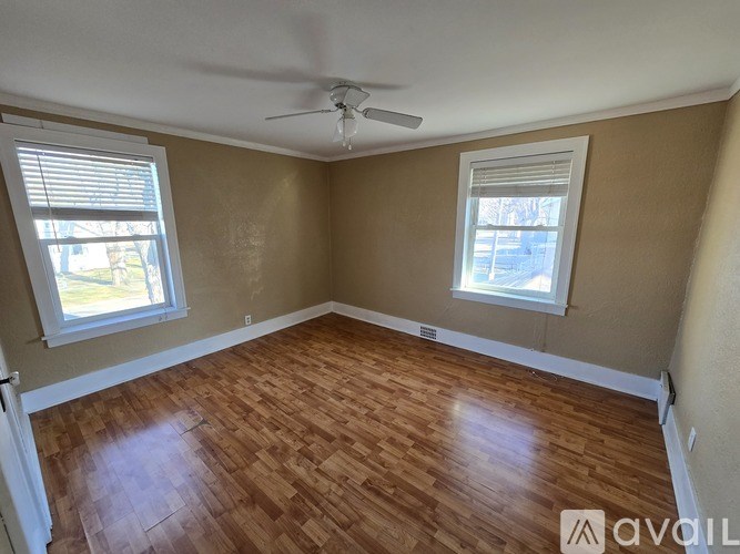 A room with wooden flooring and two windows.