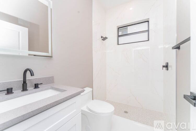 A white toilet sits in a bathroom with a marble countertop and a large mirror above it.