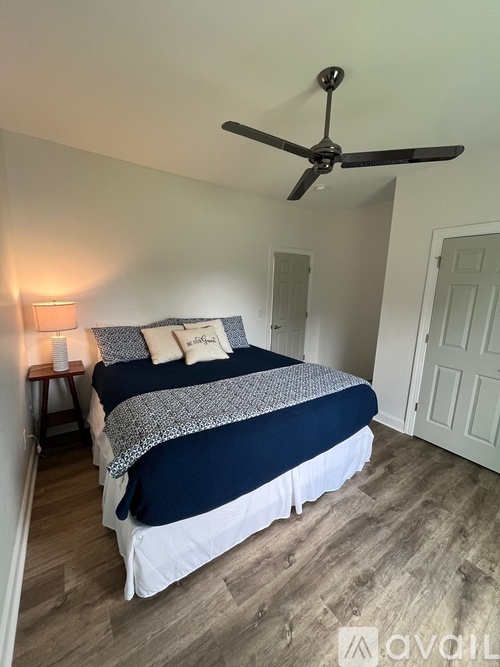 A bedroom with a bed, a ceiling fan, and a nightstand with a lamp.