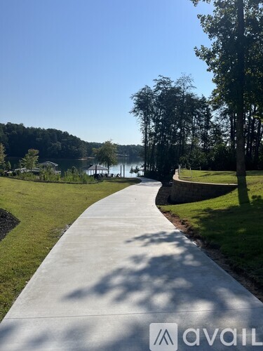 A concrete walkway leads through a grassy area with trees and a body of water in the distance.
