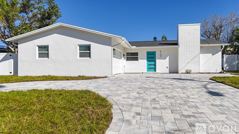 A white house with a blue door and a grey driveway.