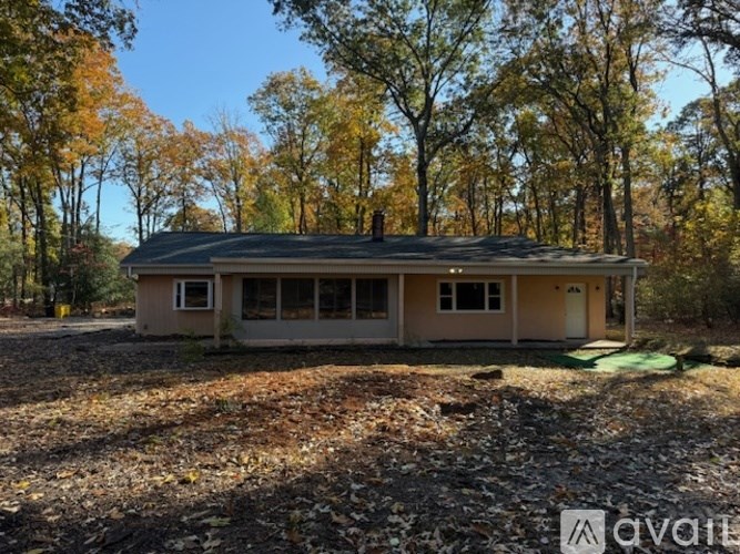 A house with a brown roof and beige walls is surrounded by trees with orange leaves.