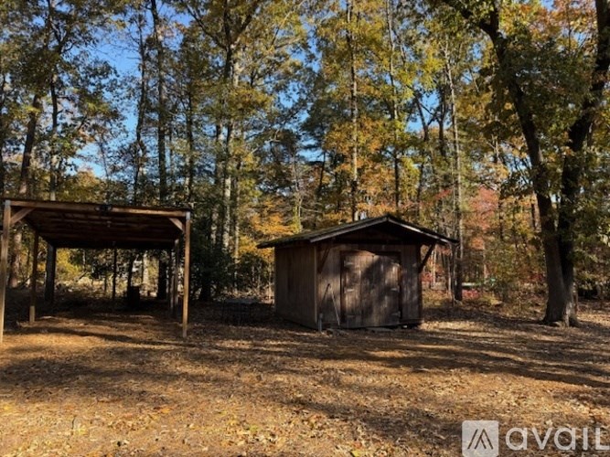 A small wooden shed sits in a field with trees in the background.