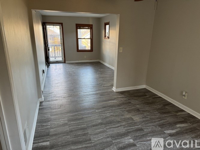 A spacious room with wood flooring and two windows.