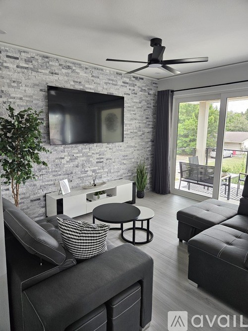 A modern living room with a black sofa, a white coffee table, and a flat-screen TV mounted on a brick wall.