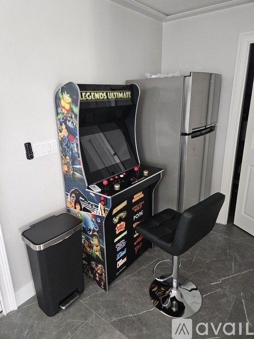 A Legends Ultimate pinball machine sits in a room with a black chair and trash can.