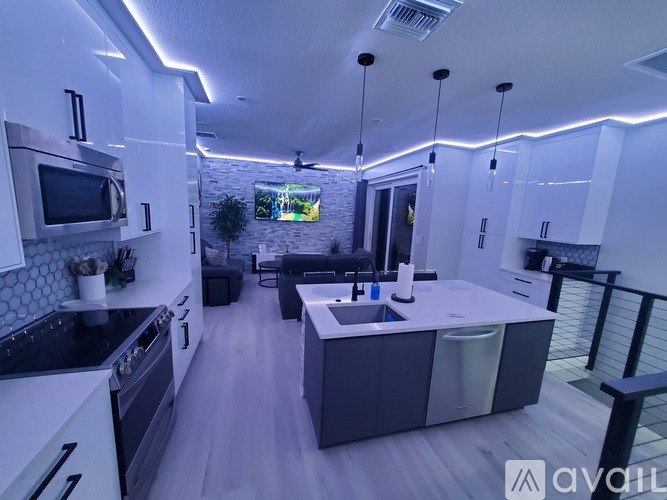 A modern kitchen with a black countertop and stove, white cabinets, and a TV mounted on the wall.