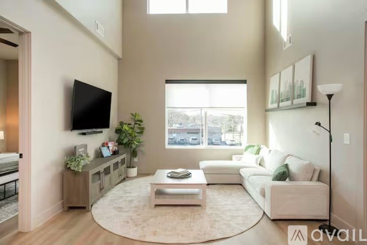 A living room with a white couch, a coffee table, and a flat-screen TV mounted on the wall.