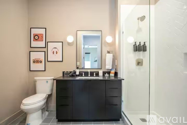 A bathroom with a white toilet, black vanity, and a glass shower door.