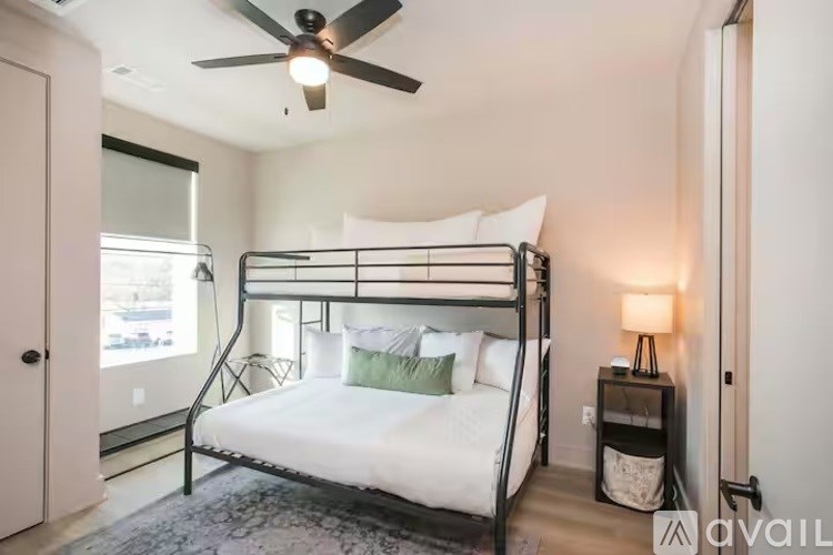 A bedroom with a metal frame bed, a ceiling fan, and a small table with a lamp.