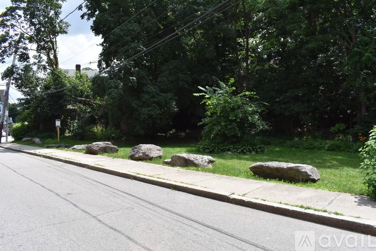 A street with a sidewalk and a grassy area with rocks.