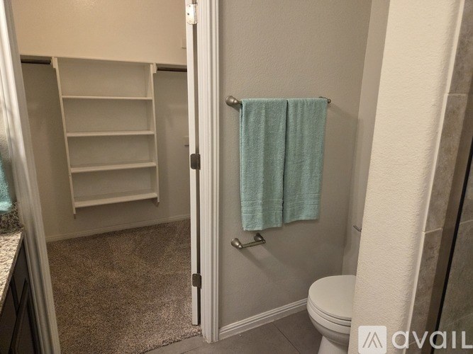 A bathroom with a toilet, a shower with a blue towel hanging on the side, and a white shelving unit.
