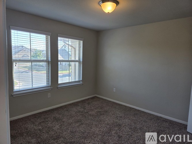 A room with a carpeted floor, two windows with blinds, and a ceiling light fixture.