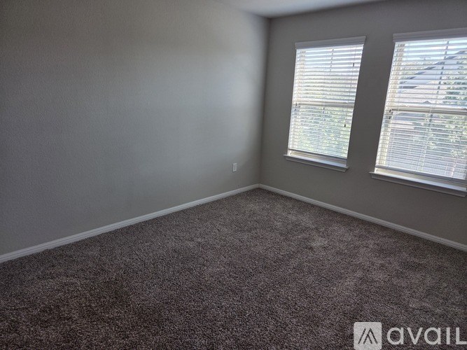 A room with grey carpet and two windows with blinds.