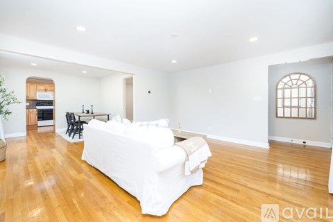 A large white couch sits in a spacious living room with wooden floors and white walls.